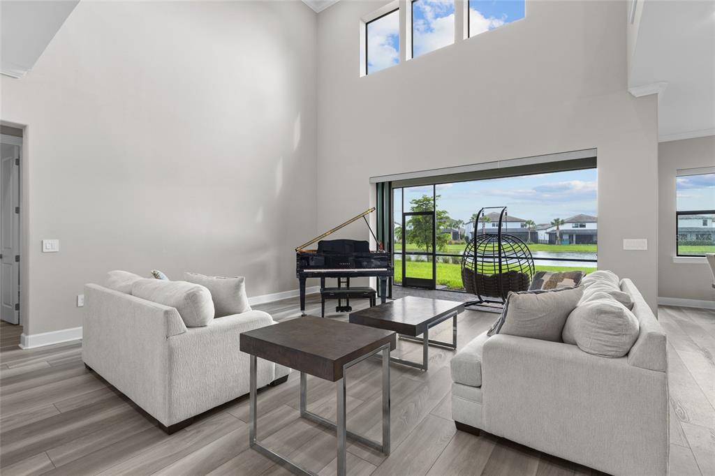 A living room with high ceilings, a grand piano, and a view of a lake — 5855 SILVERSIDE PINE COURT, LAKEWOOD RANCH, FL