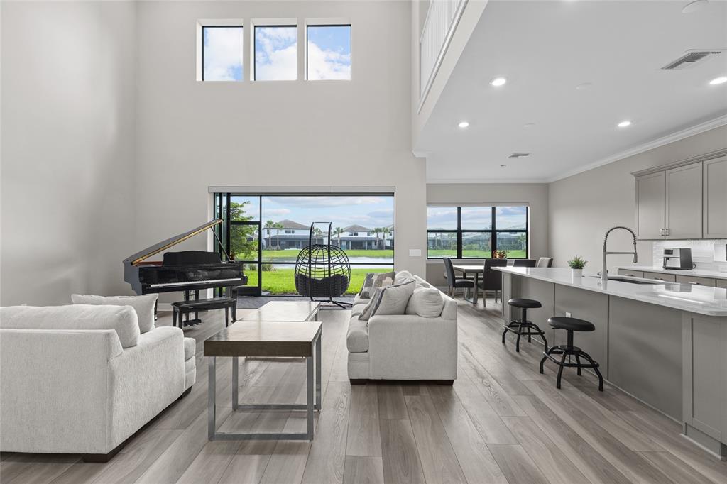 An open-concept living room and kitchen featuring a grand piano, light flooring, and large windows — 5855 SILVERSIDE PINE COURT, LAKEWOOD RANCH, FL