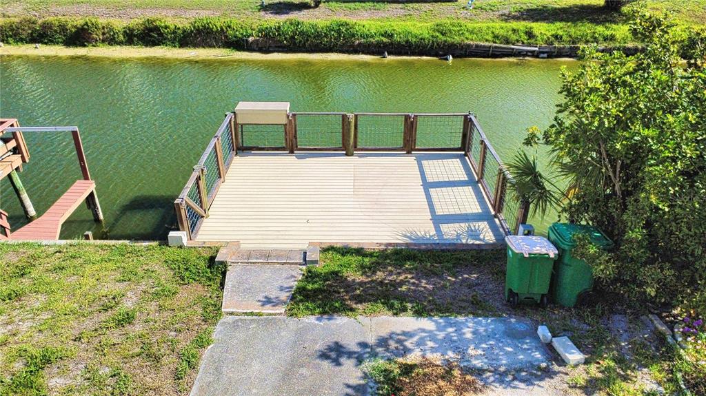 A wooden deck with metal railings overlooks a canal next to two green trash bins — 1475 FLAMINGO DRIVE UNIT 389, ENGLEWOOD, FL