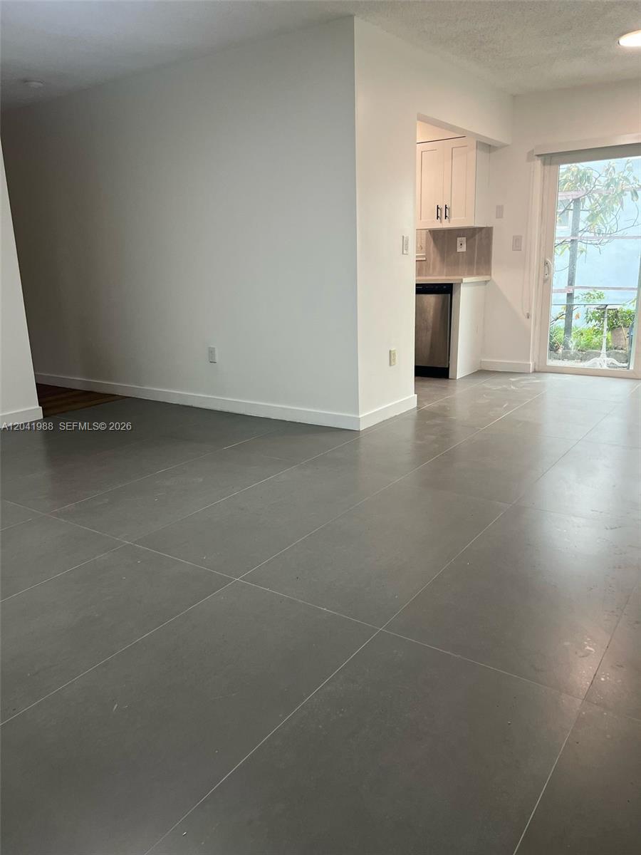 A room with large gray floor tiles leads to a kitchen and a glass door — 2611 NE 204th Ter, Miami FL 33180, MIAMI, FL