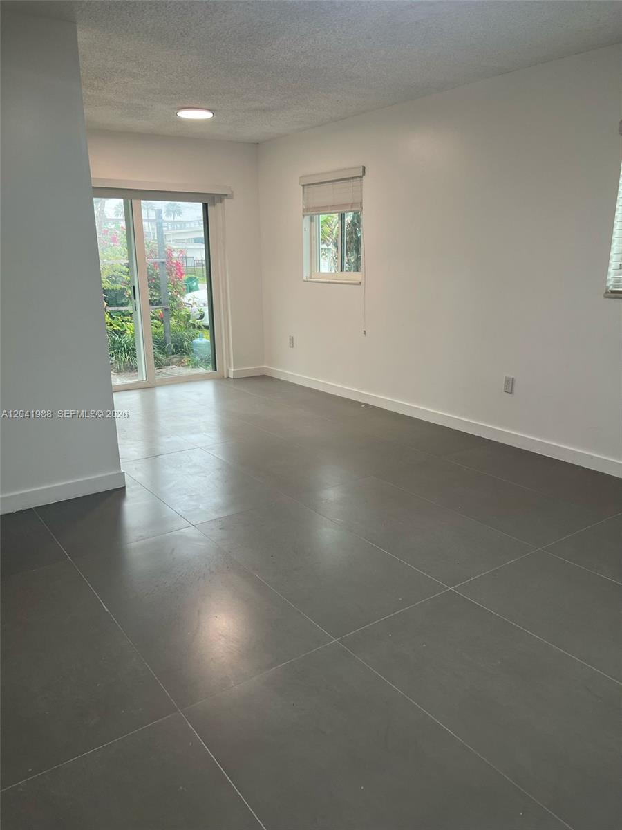 An empty room features gray tile flooring, white walls, and a sliding glass door — 2611 NE 204th Ter, Miami FL 33180, MIAMI, FL