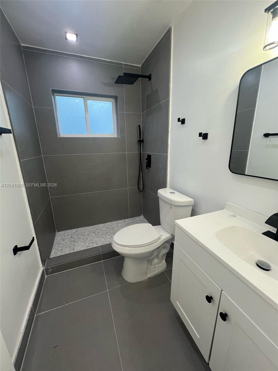 A modern bathroom features a walk-in shower with gray tile, a white vanity, and a toilet — 2611 NE 204th Ter, Miami FL 33180, MIAMI, FL
