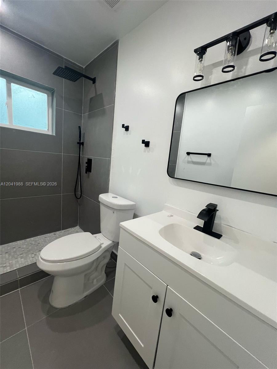 A modern bathroom features a white vanity, a toilet, and a tiled walk-in shower — 2611 NE 204th Ter, Miami FL 33180, MIAMI, FL