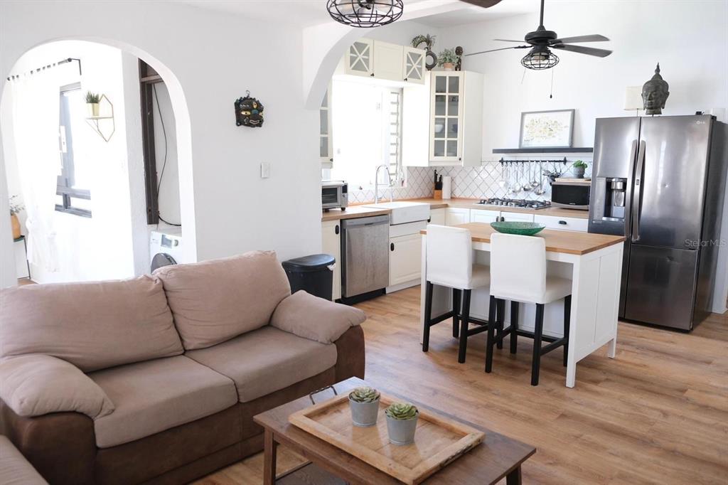 A living room with a brown sofa faces an open kitchen featuring white cabinets and an island — 200 SOL ST. UNIT PH-D1, OLD SAN JUAN, PR