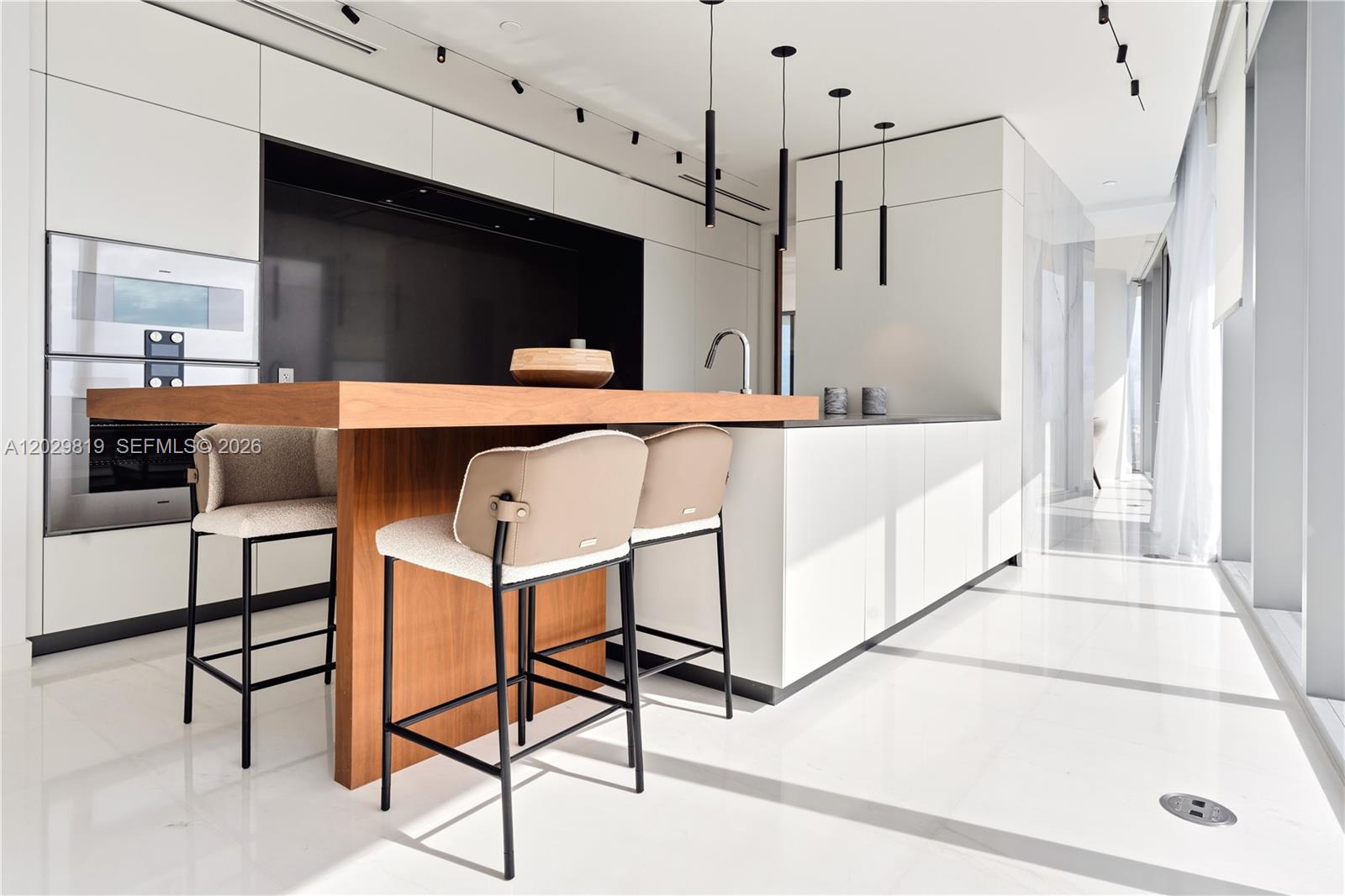 A modern kitchen features a wooden breakfast bar, white cabinetry, and black pendant lighting — 300 E Biscayne Blvd Way # 5101, Miami FL 33131, MIAMI, FL