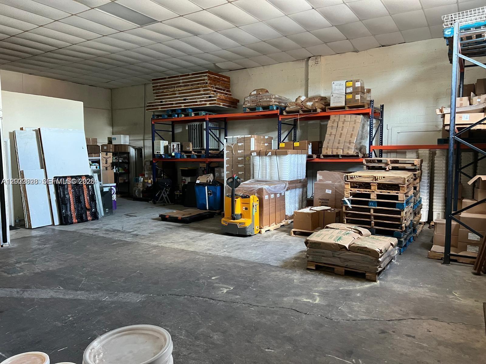 A warehouse interior features industrial shelving units, stacked pallets, and a yellow electric pallet jack — 1950 Hayes St, Hollywood FL 33020, HOLLYWOOD, FL