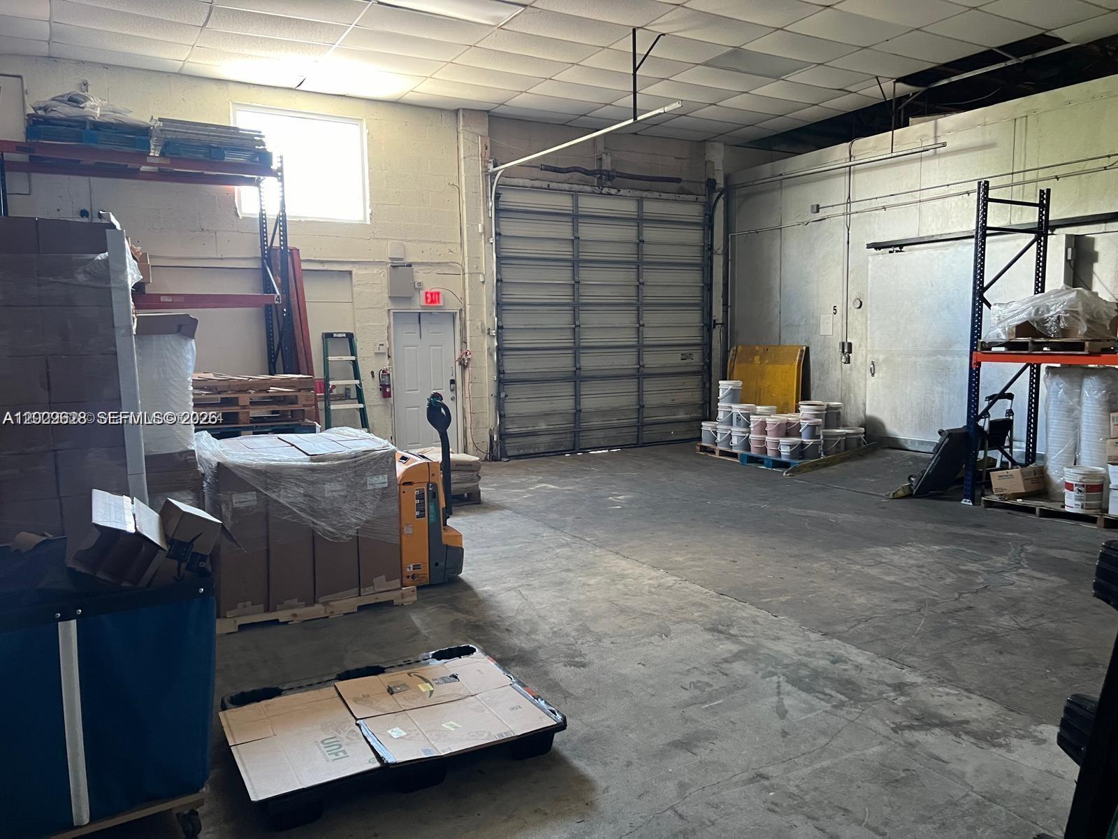 A warehouse interior features a large roll-up door, concrete floors, and industrial storage racking — 1950 Hayes St, Hollywood FL 33020, HOLLYWOOD, FL