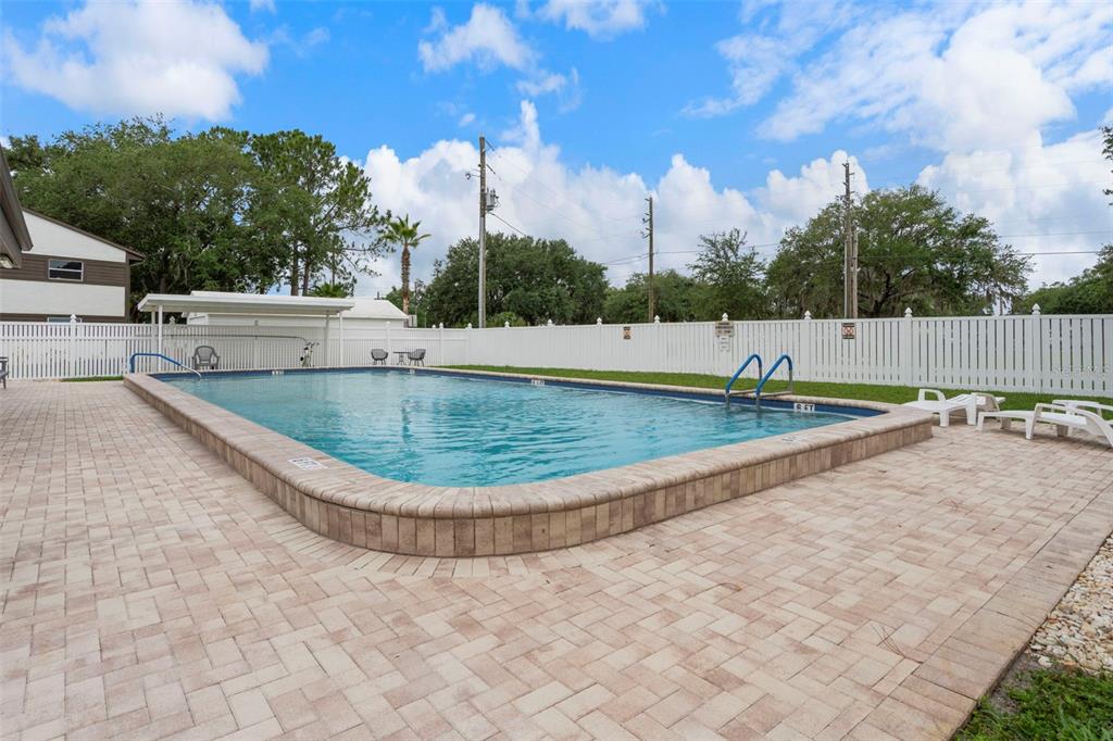 An outdoor rectangular swimming pool with a brick paver deck and white vinyl fence — 4101 PASSPORT LANE UNIT 202, NEW PORT RICHEY, FL