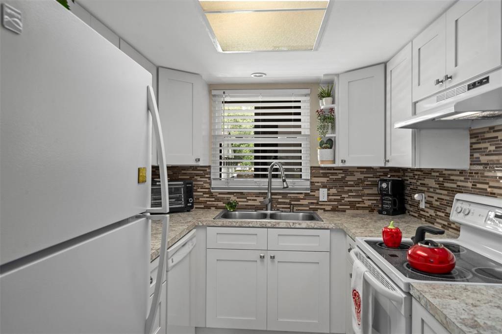 A galley kitchen features white cabinets, a mosaic tile backsplash, and a double-basin sink — 4101 PASSPORT LANE UNIT 202, NEW PORT RICHEY, FL