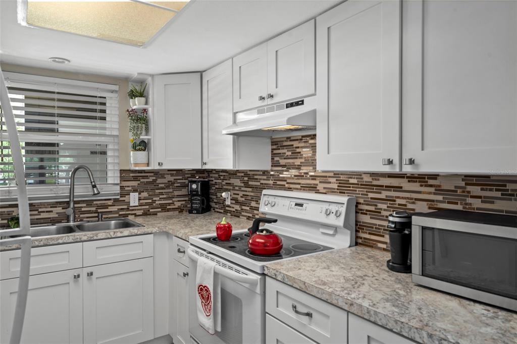 A kitchen features white cabinets, a mosaic tile backsplash, laminate countertops, and a white stove — 4101 PASSPORT LANE UNIT 202, NEW PORT RICHEY, FL