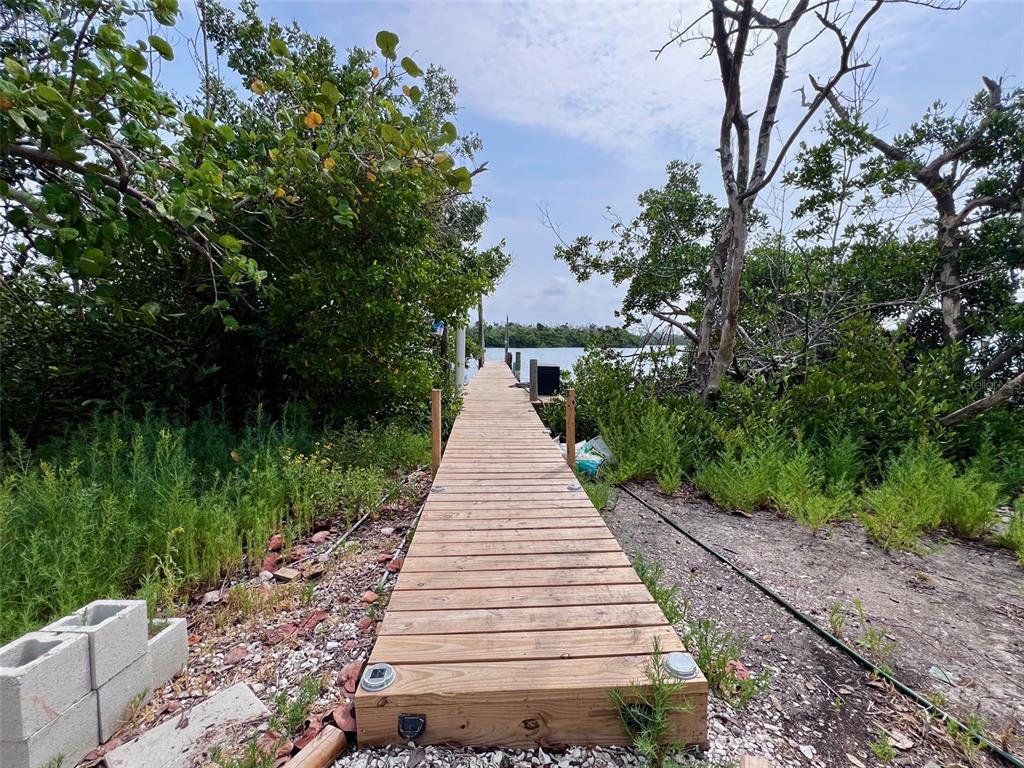 A wooden dock extends from a dirt path toward the water surrounded by trees — 8146 LITTLE GASPARILLA ISLAND, PLACIDA, FL
