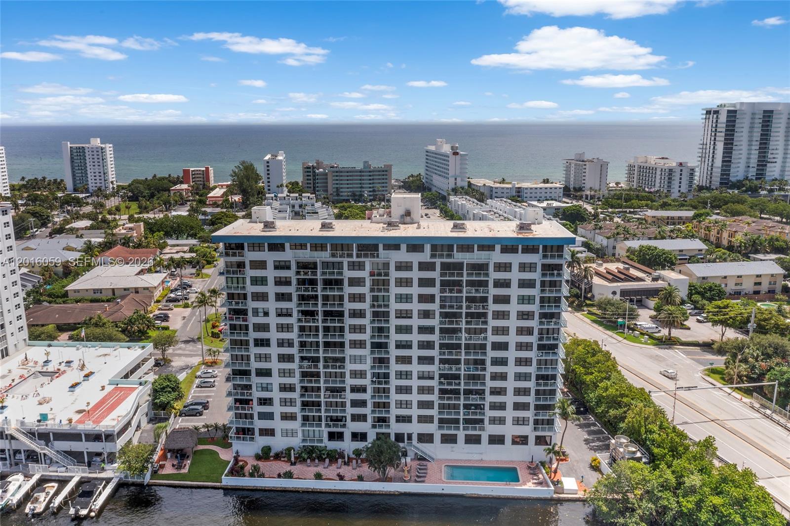 An aerial view shows a tall residential building with a pool beside a waterway — 1401 N Riverside Dr # 1406, Pompano Beach FL 33062, POMPANO BEACH, FL
