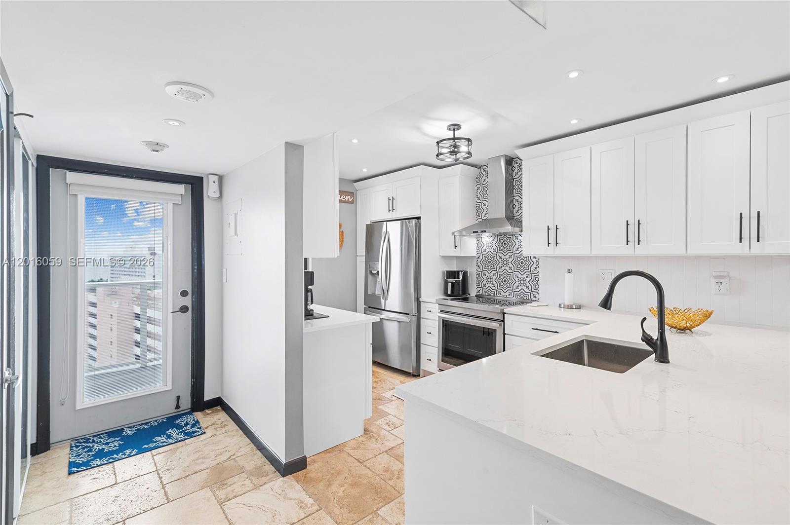 A modern kitchen features white cabinets, stainless steel appliances, a patterned backsplash, and stone flooring — 1401 N Riverside Dr # 1406, Pompano Beach FL 33062, POMPANO BEACH, FL