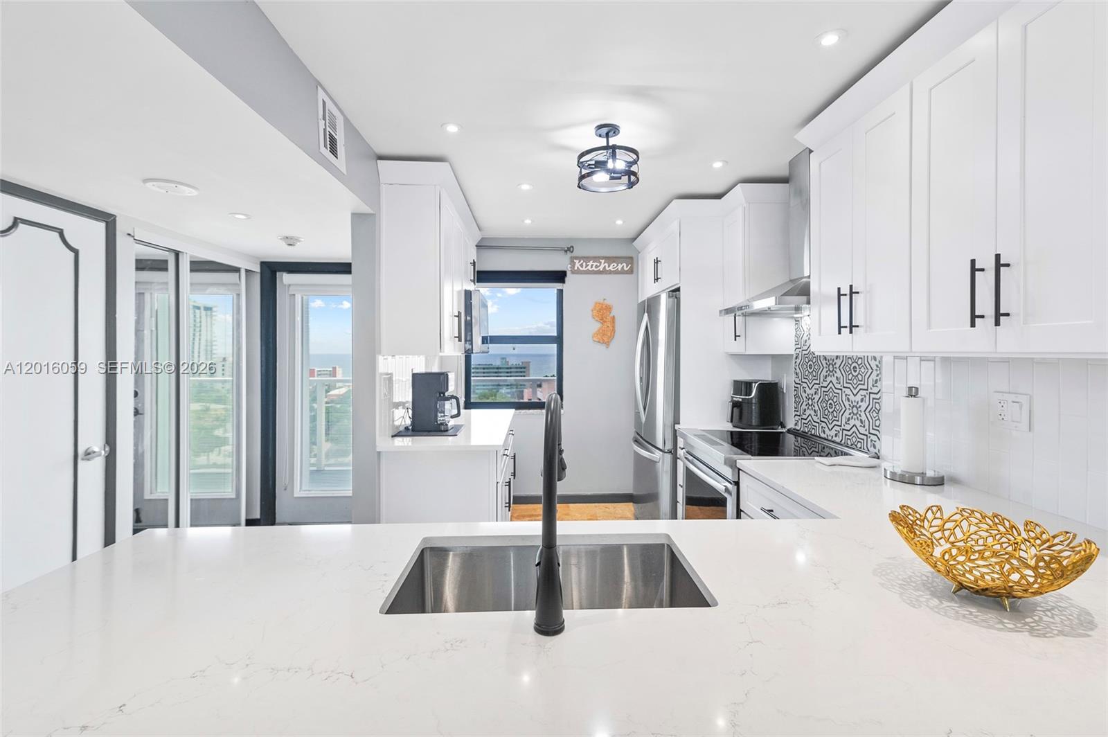 A modern kitchen features white cabinets, quartz countertops, a stainless steel sink, and ocean views — 1401 N Riverside Dr # 1406, Pompano Beach FL 33062, POMPANO BEACH, FL