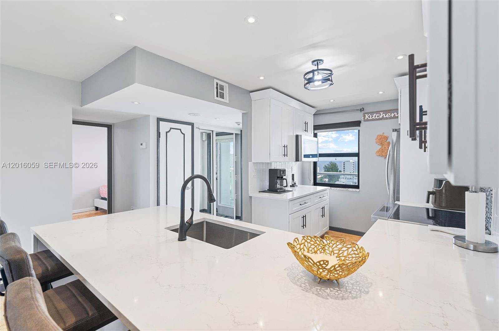 A modern kitchen features white cabinets, quartz countertops, a central island, and a window view — 1401 N Riverside Dr # 1406, Pompano Beach FL 33062, POMPANO BEACH, FL