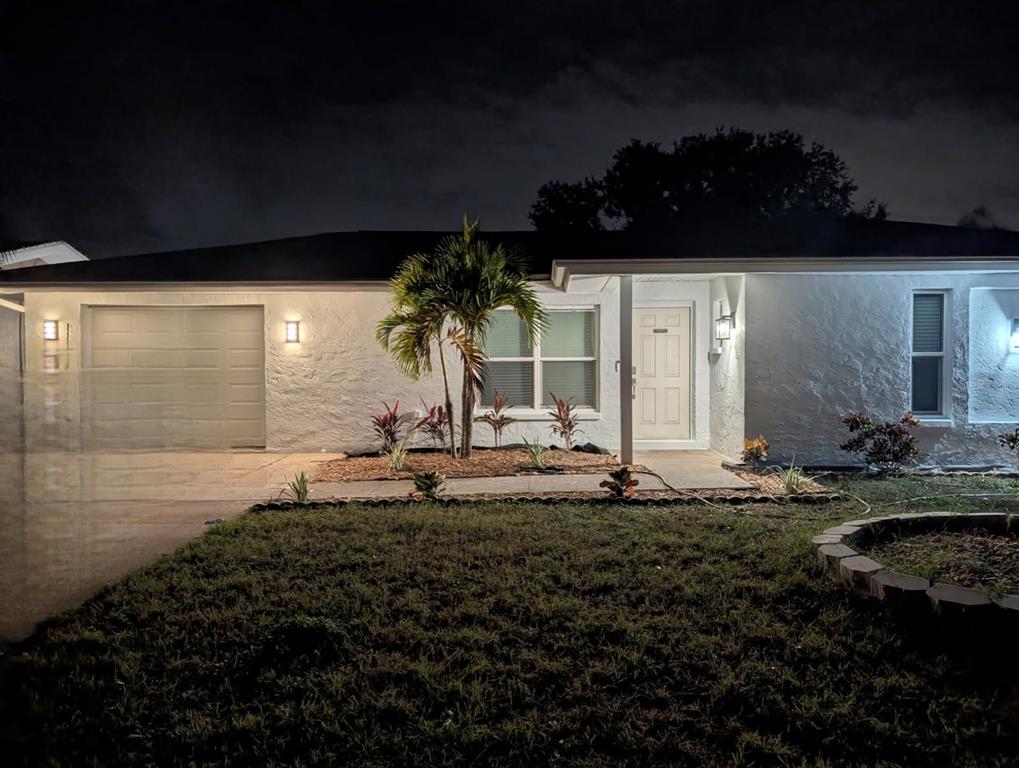 A single-story white house with a garage, palm tree, and exterior lighting at night — 1705 IRONWOOD COURT E, OLDSMAR, FL