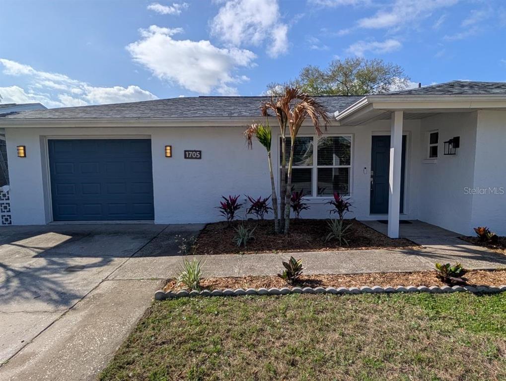 A single-story white house features a blue garage door, a front porch, and landscaping — 1705 IRONWOOD COURT E, OLDSMAR, FL