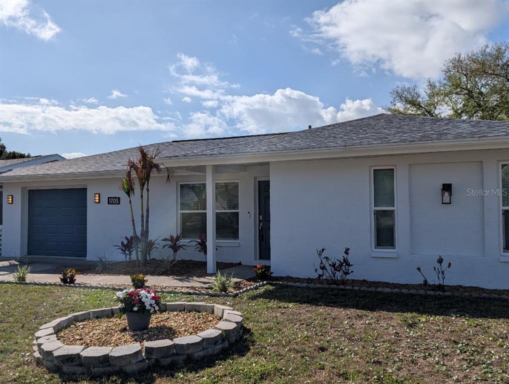 A white single-story house with a gray roof, a garage, and a stone-bordered garden bed — 1705 IRONWOOD COURT E, OLDSMAR, FL