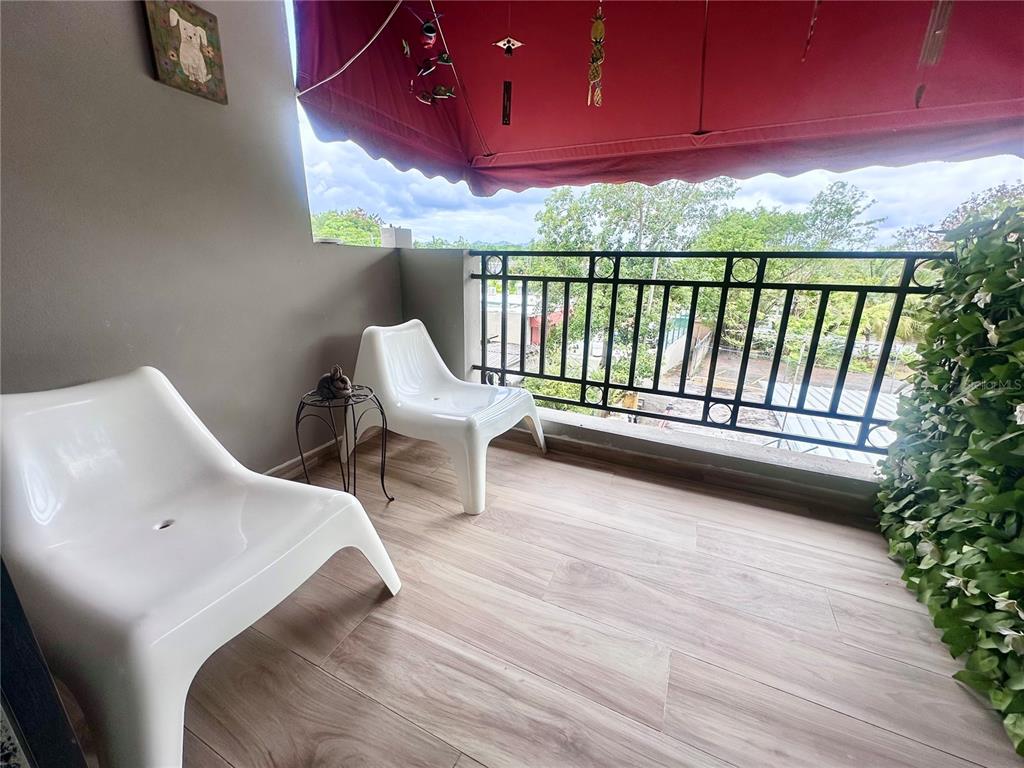 A balcony features two white chairs, a small side table, wood-look flooring, and a red awning — 24a LOPATEGUI UNIT 107a, GUAYNABO, PR