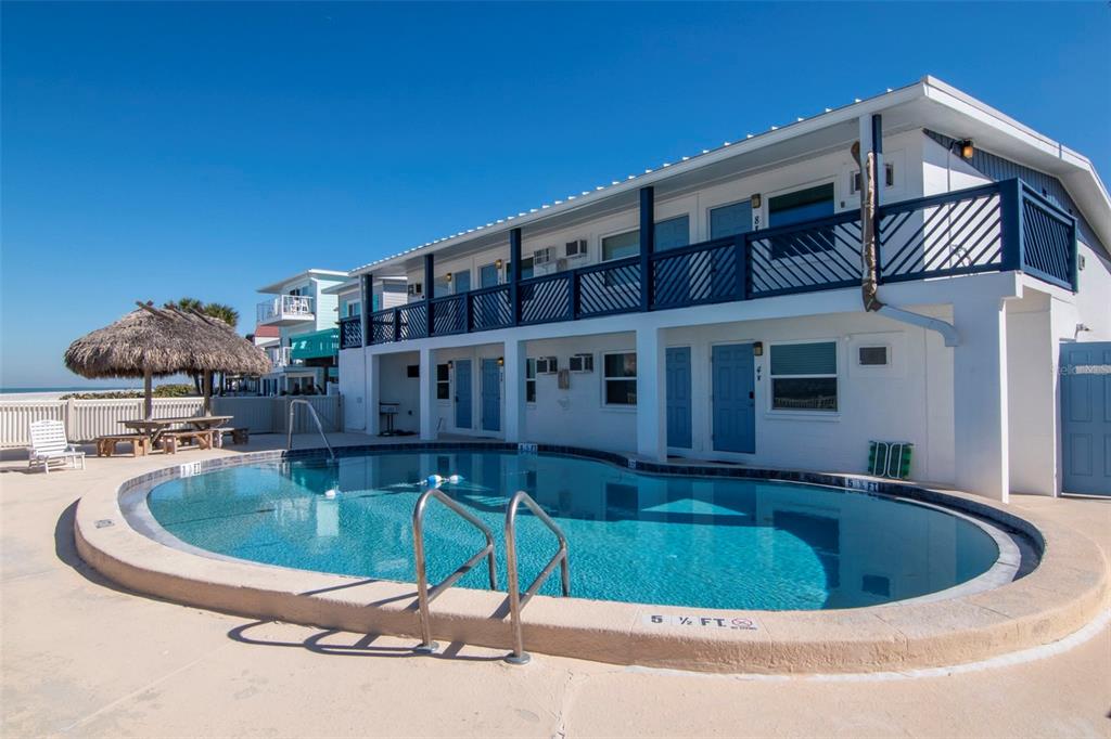 An open door reveals a swimming pool and a beach view with thatched umbrellas — 2700 GULF BOULEVARD UNIT 2W, BELLEAIR BEACH, FL