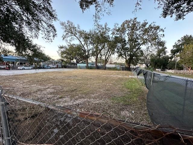 A fenced, vacant lot with sparse grass and several large trees in the background — 9330 1ST AVENUE, ORLANDO, FL