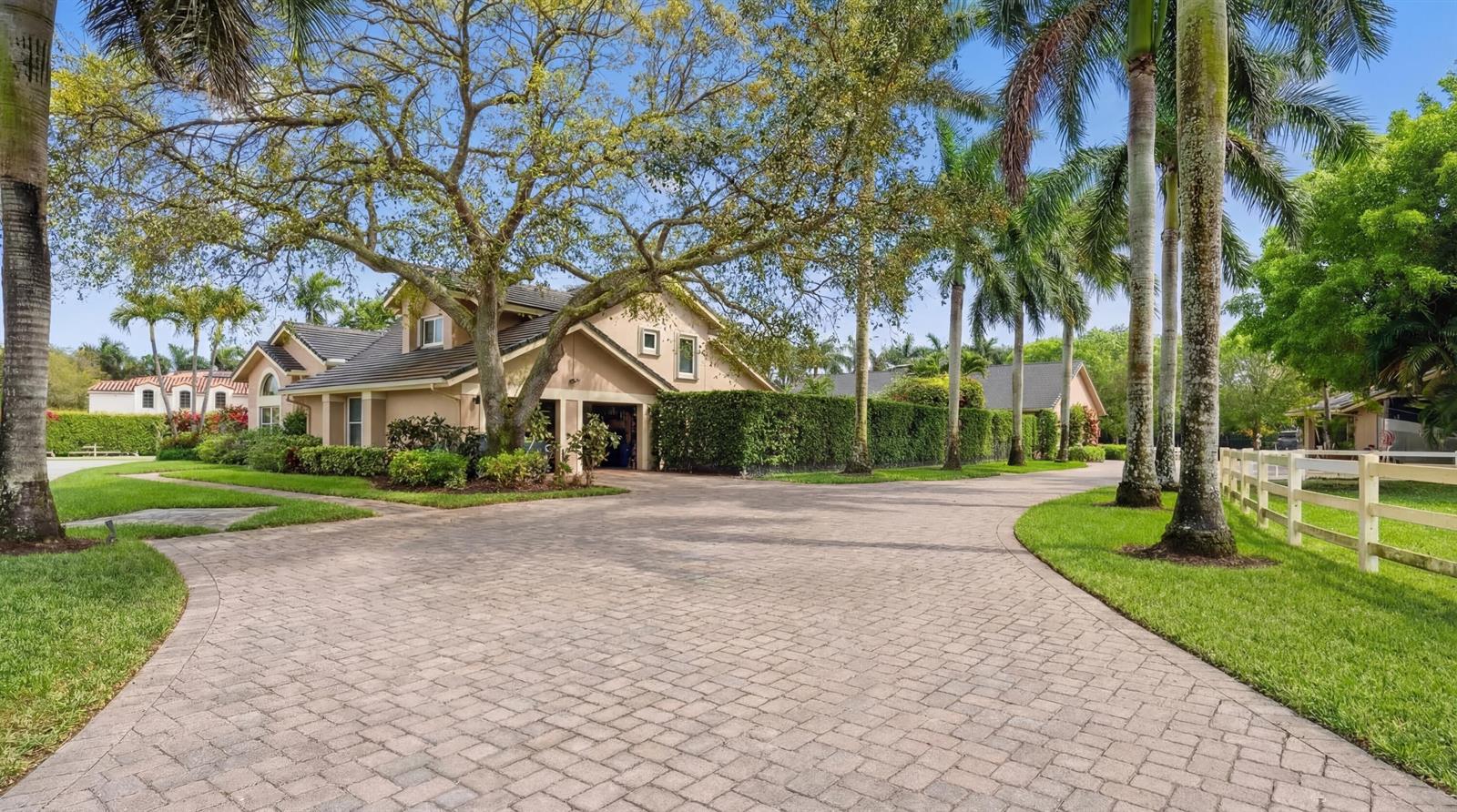 A paved driveway leads to a tan house with a garage and surrounding palm trees — 14911 Equestrian Way, Wellington FL 33414, WELLINGTON, FL
