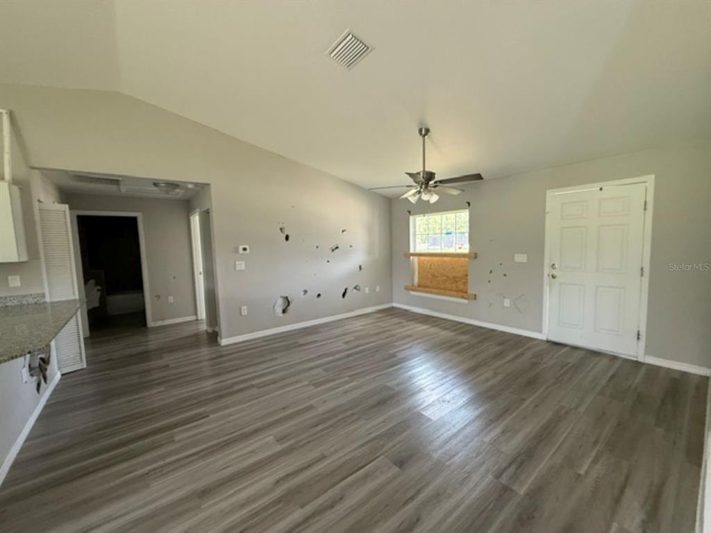 A living room with gray walls, wood-look flooring, a ceiling fan, and damaged wall surfaces — 2 DOGWOOD DRIVE RADL., OCALA, FL