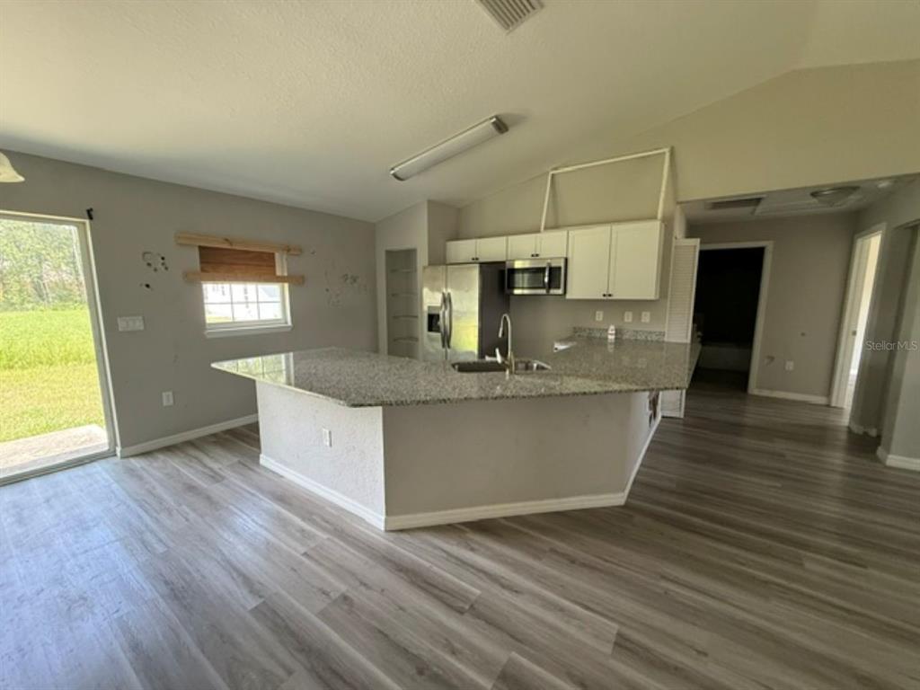 A kitchen with granite countertops, light wood-look flooring, and white cabinets opens to a living area — 2 DOGWOOD DRIVE RADL., OCALA, FL