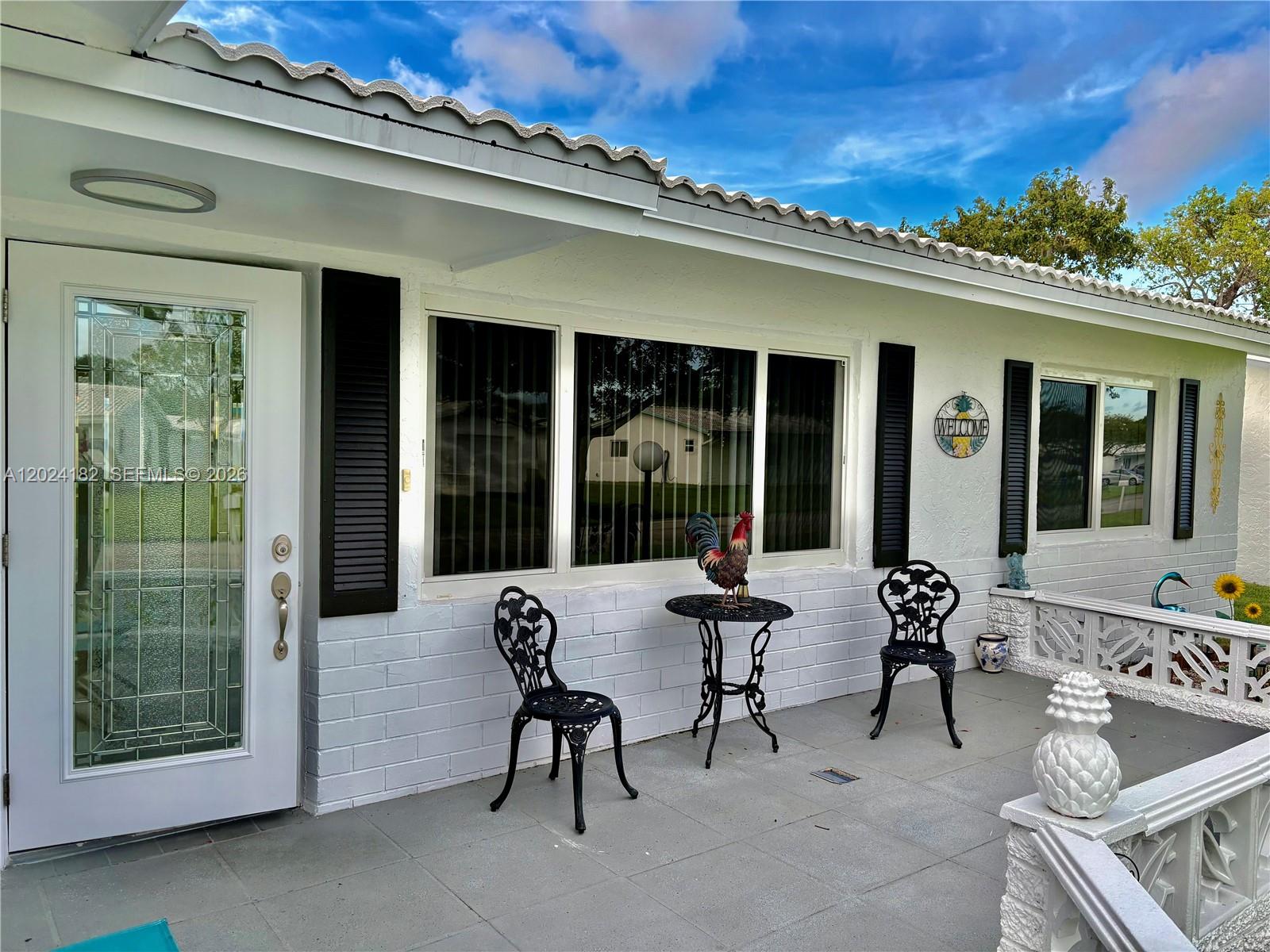 A white house exterior features a front porch with two black chairs and a table — 8225 NW 12th Ct, Plantation FL 33322, PLANTATION, FL