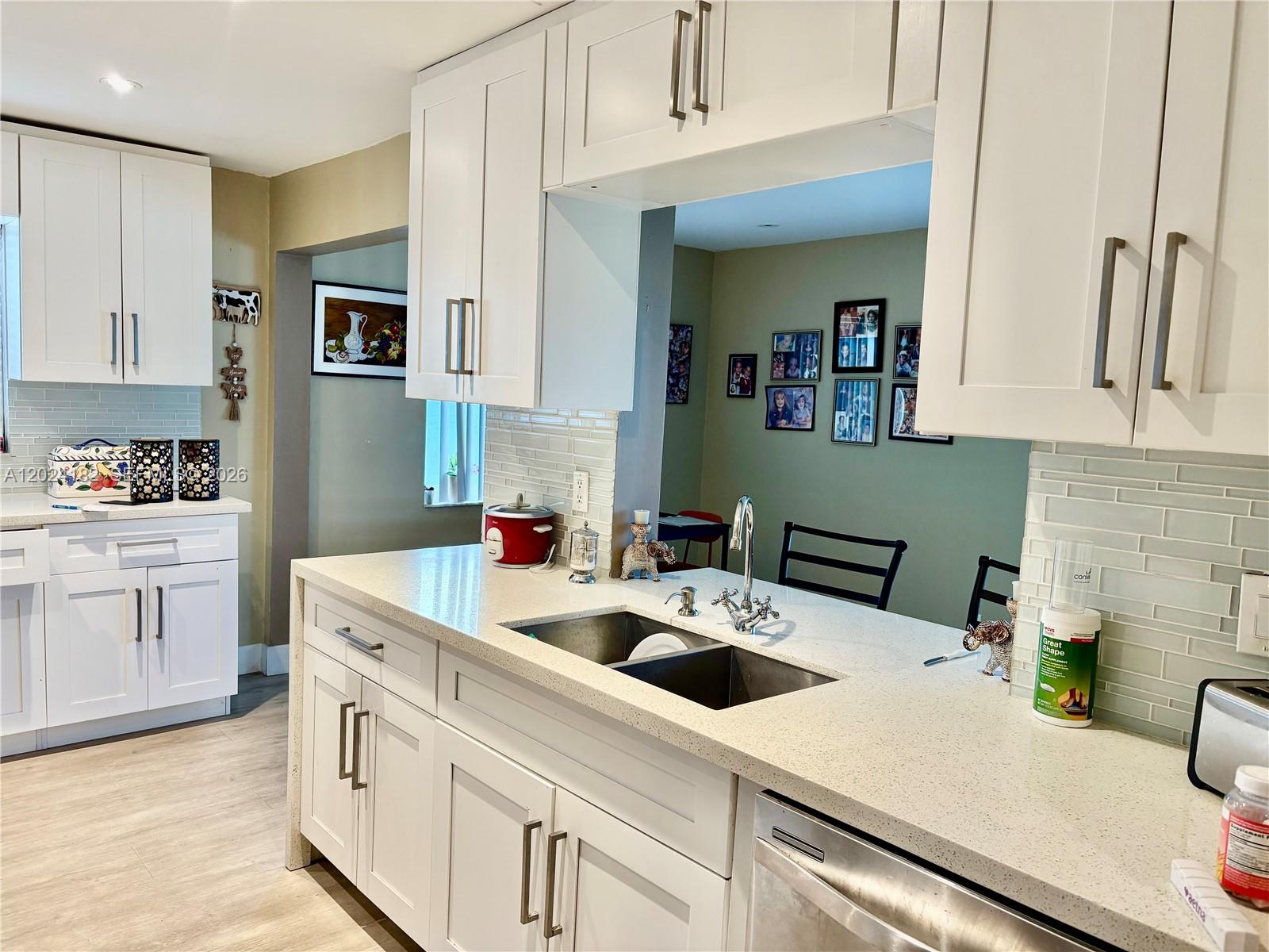 A kitchen features white cabinets, light countertops, a stainless steel sink, and a pass-through window — 8225 NW 12th Ct, Plantation FL 33322, PLANTATION, FL