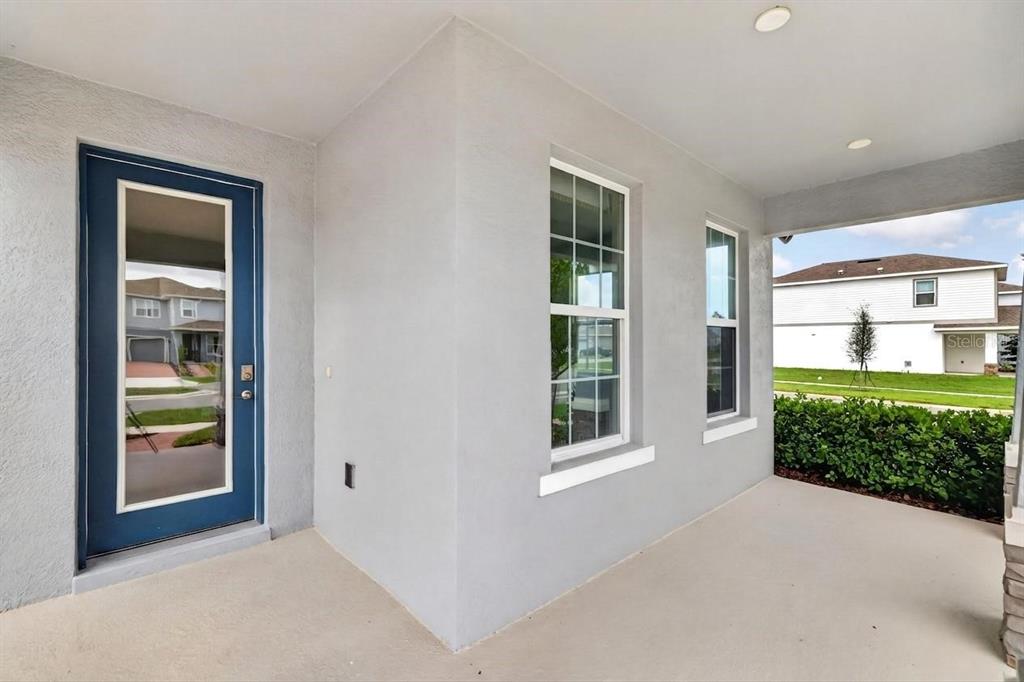 A covered concrete porch features a blue-framed glass door and two windows on a gray wall — 3894 CAPITAL REEF WAY, APOPKA, FL