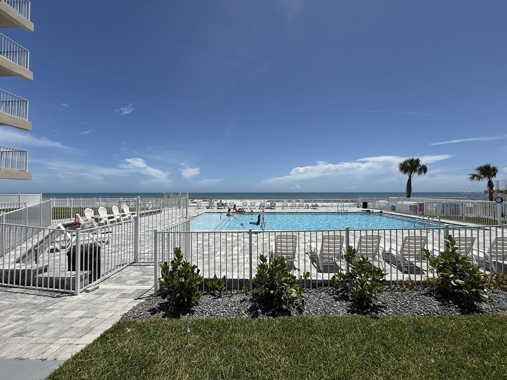 A swimming pool area with lounge chairs overlooks the ocean next to a multi-story building — 2043 S ATLANTIC AVENUE UNIT 105, DAYTONA BEACH SHORES, FL