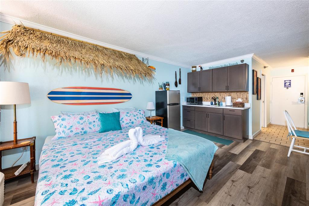 A hotel room features a bed with a surfboard wall decoration and a kitchenette area — 2043 S ATLANTIC AVENUE UNIT 105, DAYTONA BEACH SHORES, FL