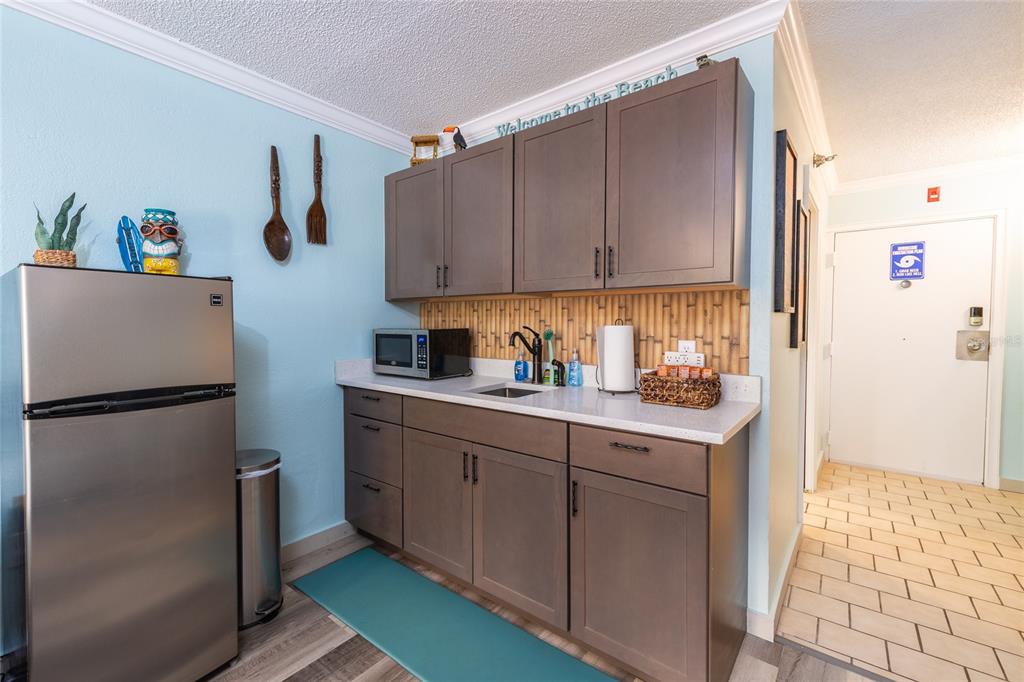 A kitchenette features dark wood cabinets, a stainless steel refrigerator, and a bamboo-patterned backsplash — 2043 S ATLANTIC AVENUE UNIT 105, DAYTONA BEACH SHORES, FL