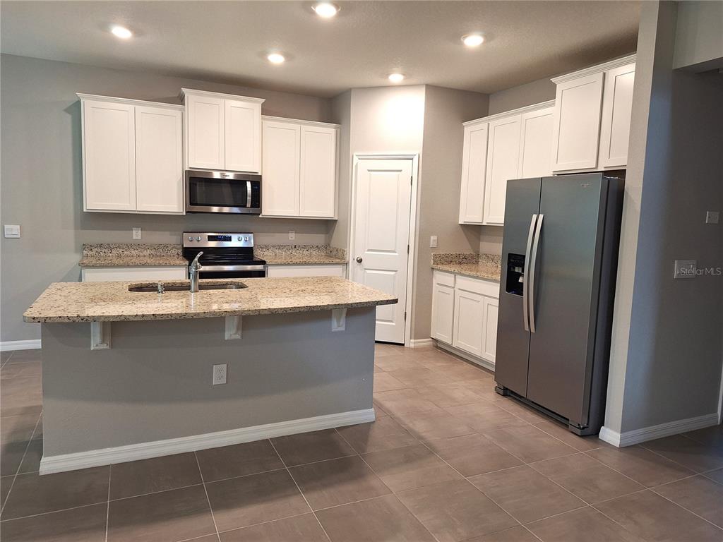 A kitchen features white cabinets, granite countertops, a center island, and stainless steel appliances — 5348 ROCKY COAST PLACE, PALMETTO, FL