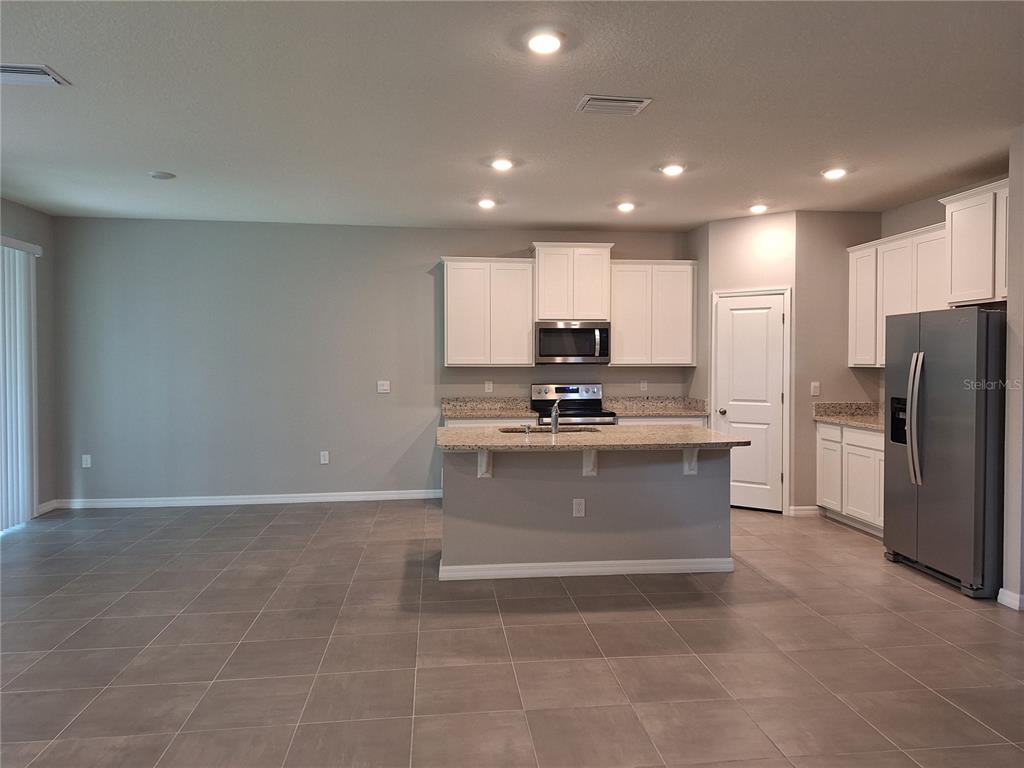 A kitchen features white cabinets, granite countertops, stainless steel appliances, and large floor tiles — 5348 ROCKY COAST PLACE, PALMETTO, FL