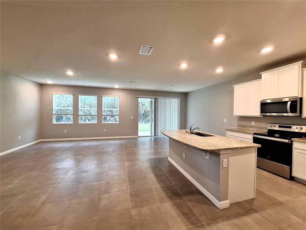 An open-concept kitchen and living area features tile flooring, granite countertops, and recessed lighting — 5348 ROCKY COAST PLACE, PALMETTO, FL