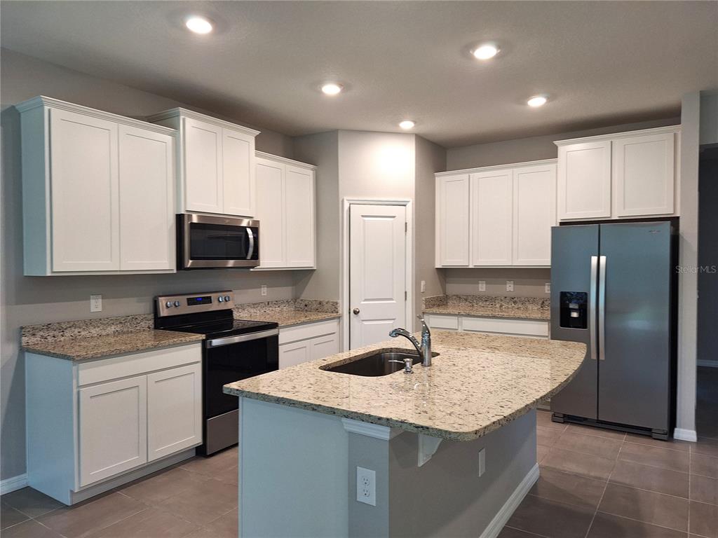 A kitchen features white cabinets, granite countertops, stainless steel appliances, and a central island — 5348 ROCKY COAST PLACE, PALMETTO, FL