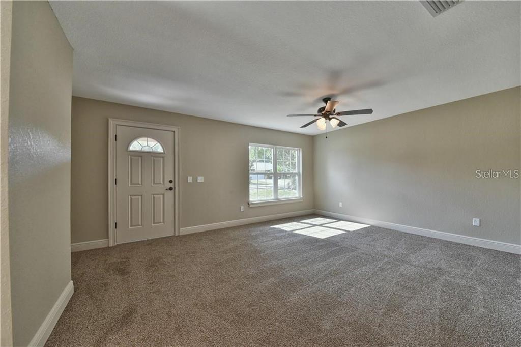 A carpeted room features a ceiling fan, a window, and an exterior door — 16025 SW 27TH AVENUE ROAD, OCALA, FL