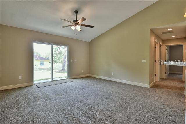 A carpeted room features a vaulted ceiling, a ceiling fan, and sliding glass doors — 16025 SW 27TH AVENUE ROAD, OCALA, FL