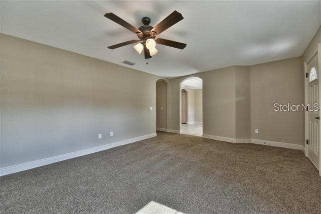 An empty room features beige walls, brown carpeting, a ceiling fan, and arched doorways — 16025 SW 27TH AVENUE ROAD, OCALA, FL