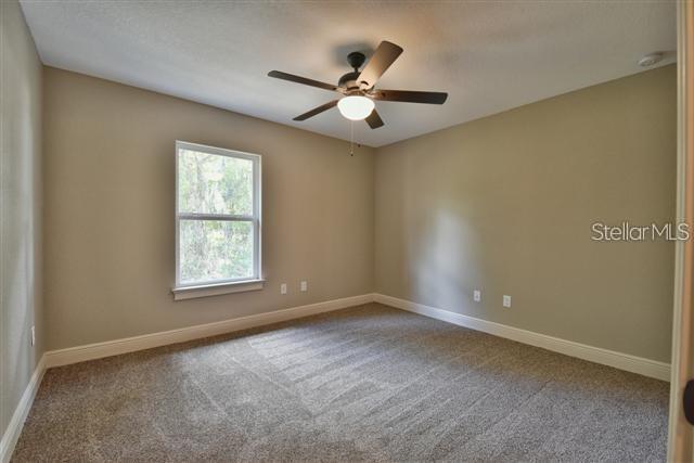 An empty bedroom features beige walls, tan carpeting, a ceiling fan, and a single window — 16025 SW 27TH AVENUE ROAD, OCALA, FL