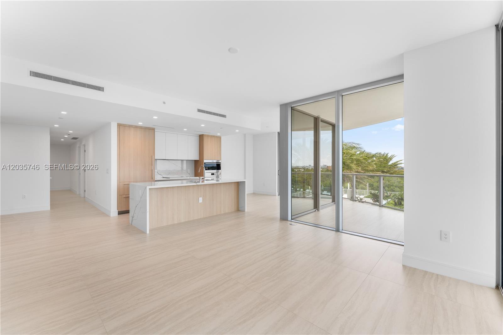 A modern open-concept kitchen and living area features light wood cabinetry and a balcony view — 2411 Laguna Circle # 705, North Miami FL 33181, NORTH MIAMI, FL