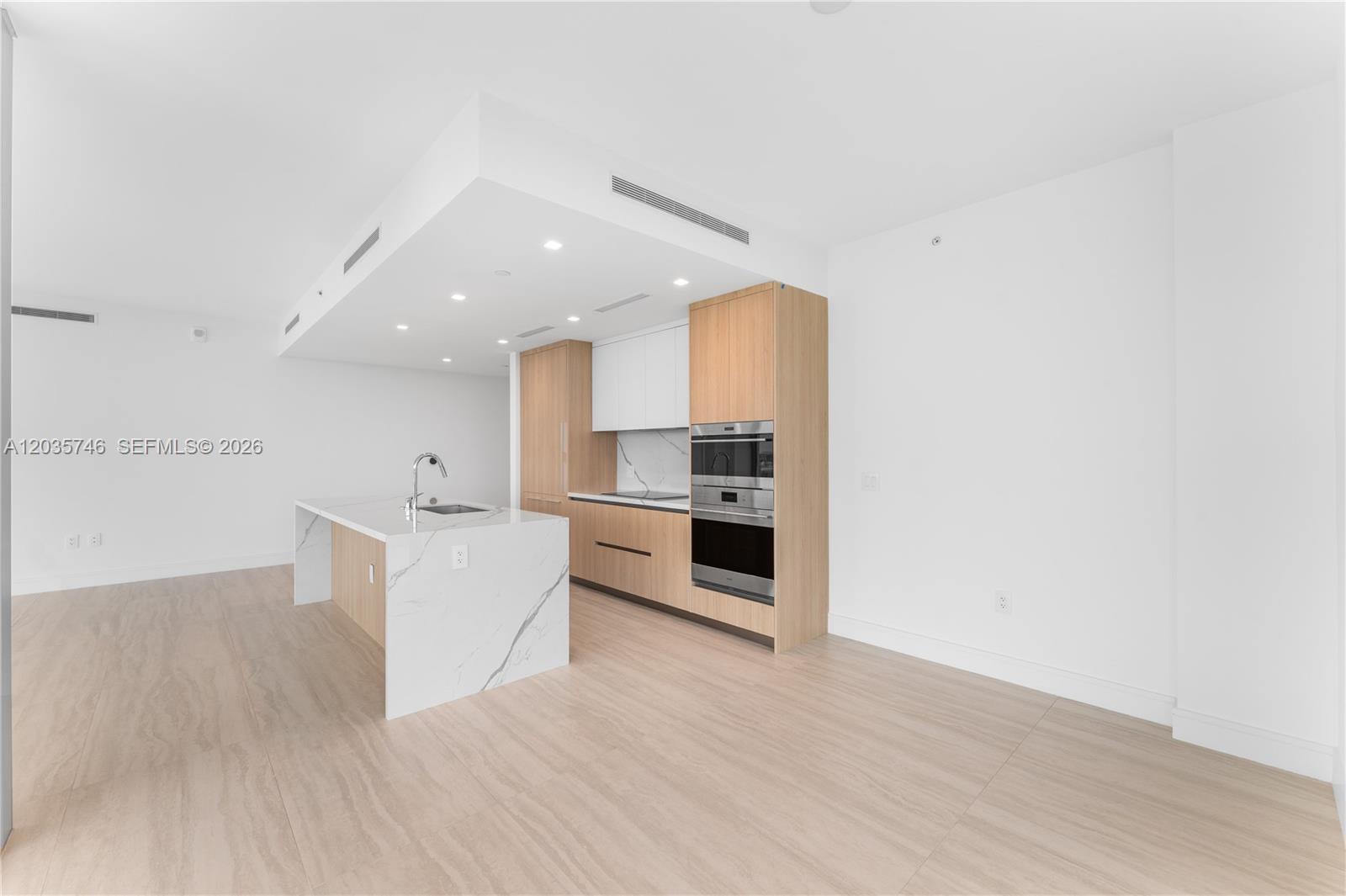 A modern kitchen features a marble-topped island, light wood cabinetry, and stainless steel appliances — 2411 Laguna Circle # 705, North Miami FL 33181, NORTH MIAMI, FL