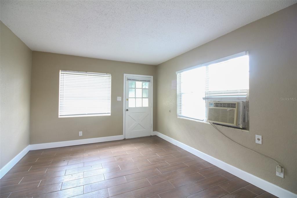 An empty room features wood-look tile flooring, beige walls, a white door, and a window unit — 1114 S TENNESSEE AVENUE, LAKELAND, FL