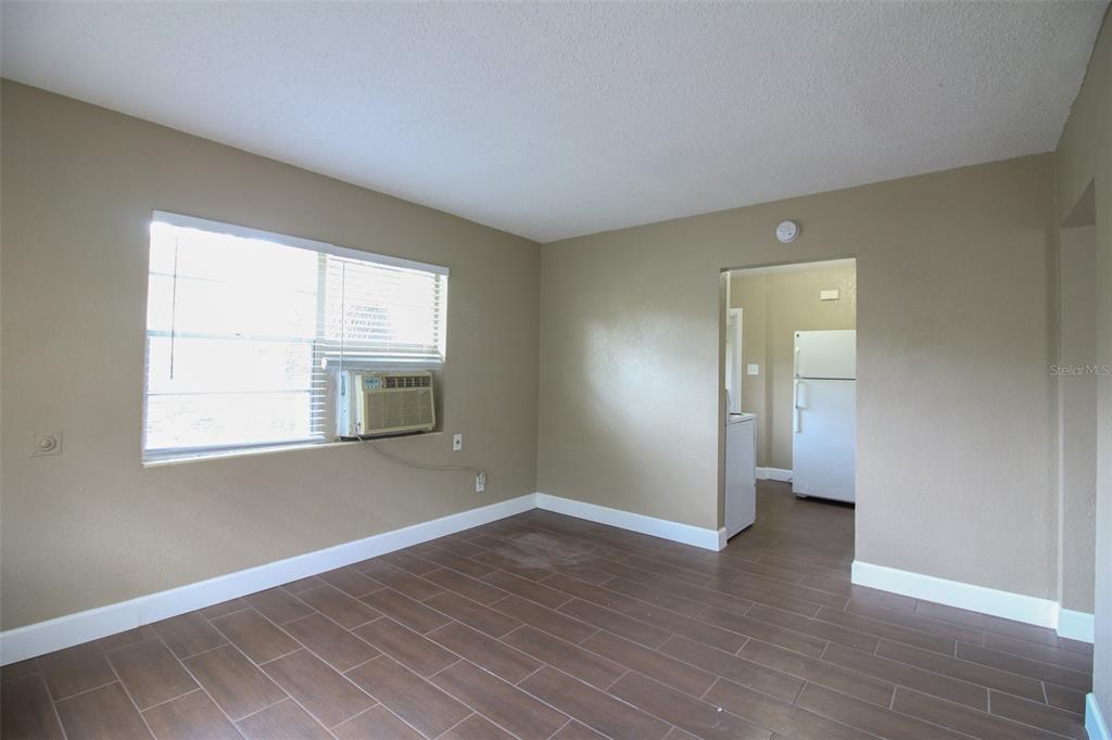 A room with tan walls, wood-look tile flooring, a window air conditioner, and a kitchen doorway — 1114 S TENNESSEE AVENUE, LAKELAND, FL
