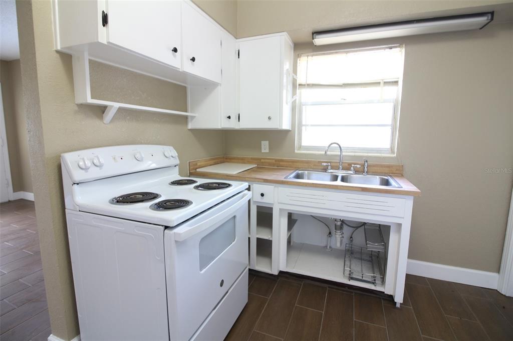 A kitchen features white cabinets, a white electric stove, and a sink with open shelving — 1114 S TENNESSEE AVENUE, LAKELAND, FL