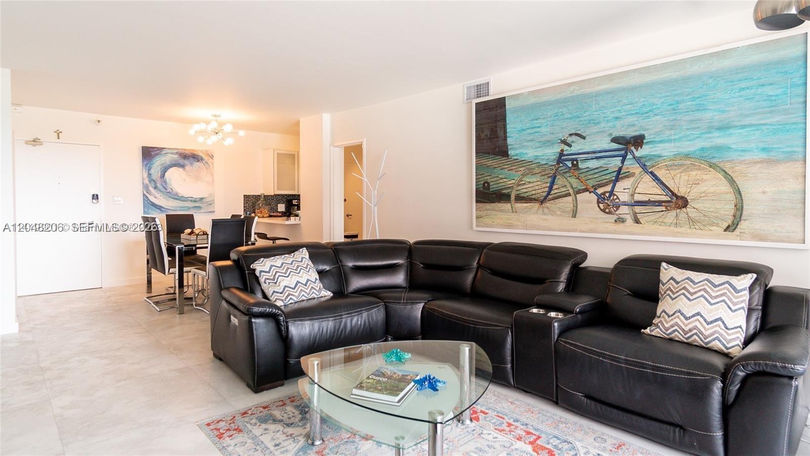 A living room features a black leather sectional sofa, a glass coffee table, and artwork — 5161 Collins Ave # 811, Miami Beach FL 33140, MIAMI BEACH, FL