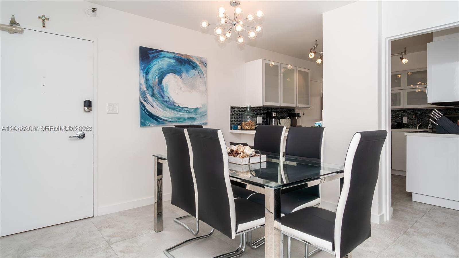 A dining area features a glass table, black chairs, and a large wave painting — 5161 Collins Ave # 811, Miami Beach FL 33140, MIAMI BEACH, FL