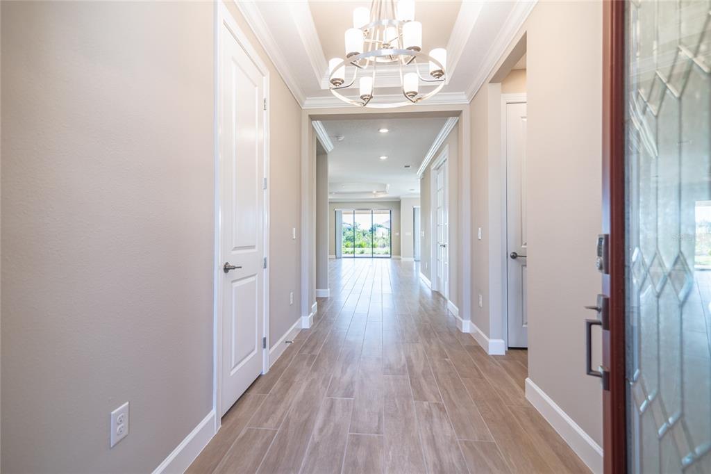 A bright foyer features wood-look tile flooring, a chandelier, and a view toward the backyard — 4798 ROSATTI ROAD, WESLEY CHAPEL, FL